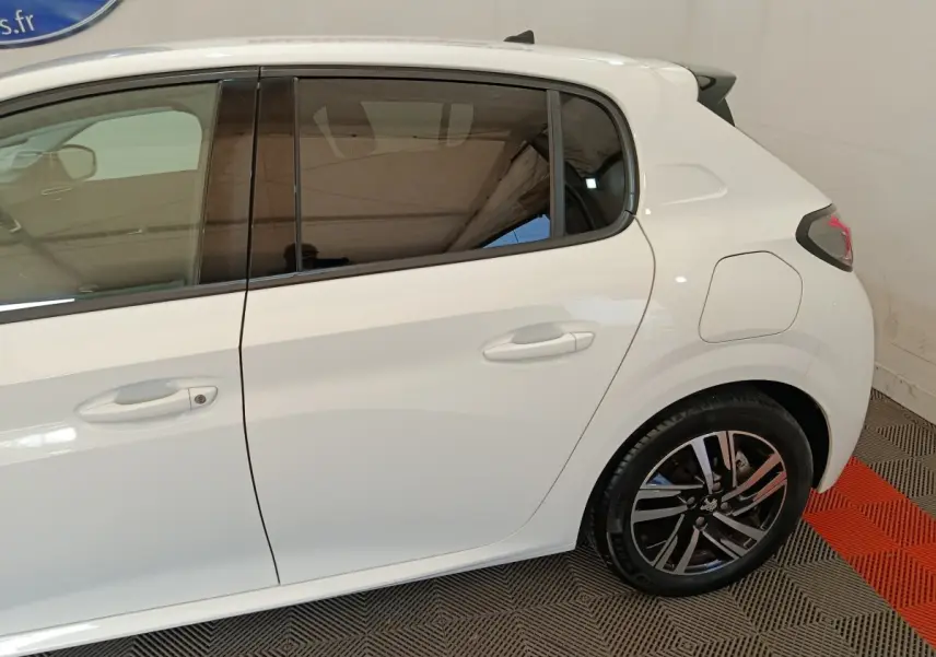 Vue latérale droite sur l'arrière d'une Peugeot 208 blanche avec jante alliage et vitres teintées.