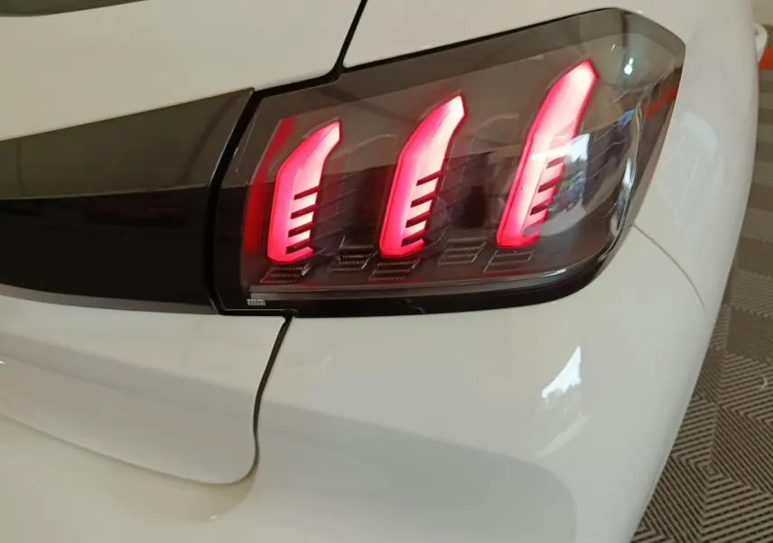 Gros plan sur le feu arrière droit rouge allumé de la Peugeot 208 blanche, version PureTech 100 S&S Allure Business.