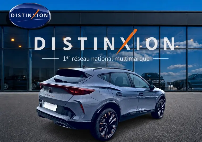 Vue 3/4 arrière droite d'une CUPRA Formentor gris graphene avec jantes noires et détails cuivrés, devant une vitrine Distinxion.