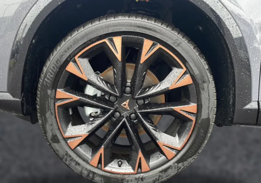 Gros plan sur la jante noire et cuivre du CUPRA Formentor gris graphene, avec pneus Bridgestone mouillés.