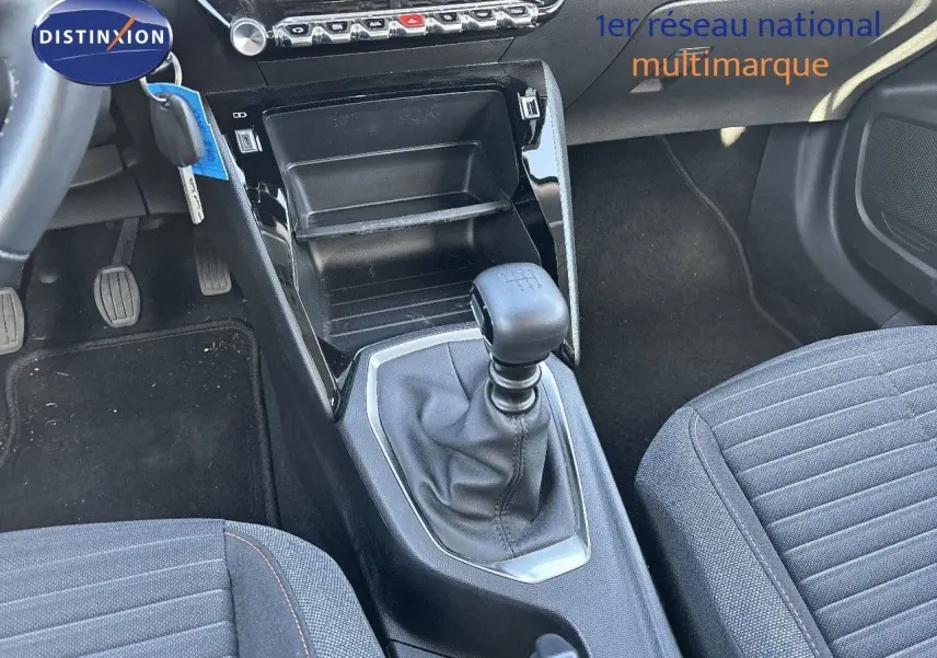 Gros plan sur la console centrale et levier de vitesse manuel d'une Peugeot 2008 gris Artense, sièges tissu noir à surpiqûres rouges.