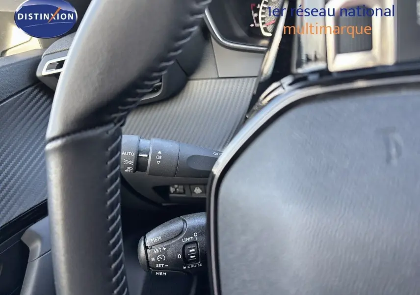 Gros plan sur le volant et les commandes de régulateur de vitesse d'une Peugeot 2008 gris Artense, intérieur noir.
