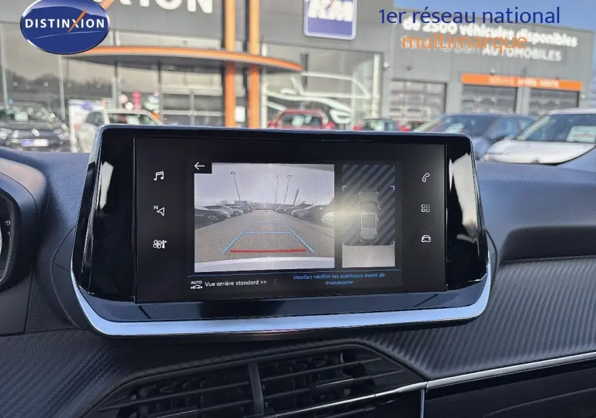 Écran tactile central affichant la caméra de recul d'un Peugeot 2008 gris, avec vue sur parking extérieur.
