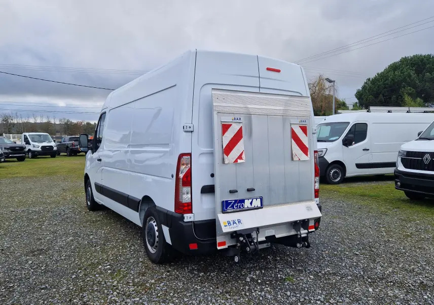 Vue 3/4 arrière droite d'un utilitaire Renault Master blanc équipé d'un hayon élévateur métallique avec marquages réfléchissants rouges.