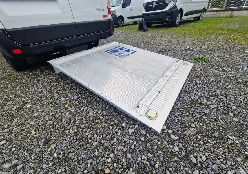 Vue arrière d'un utilitaire blanc Renault Master 2023 avec hayon déployé sur sol gravillonné.