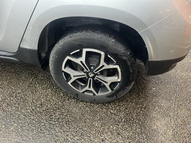 Gros plan sur la roue arrière droite d'un Dacia Duster gris Comète métallisé avec jante alu au design moderne.