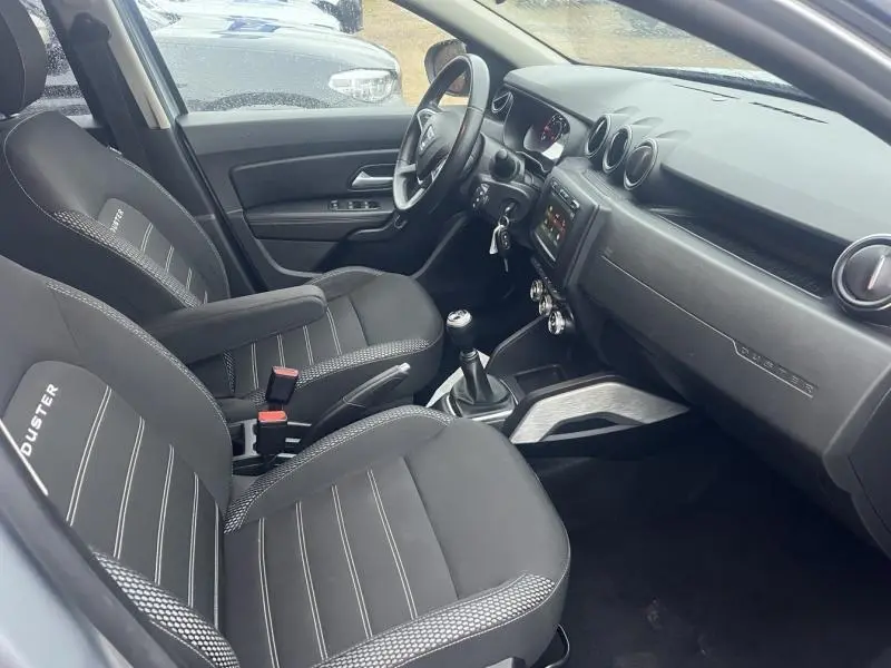 Vue intérieure côté conducteur du Dacia Duster 2021, sièges noirs avec logo Duster et tableau de bord moderne.