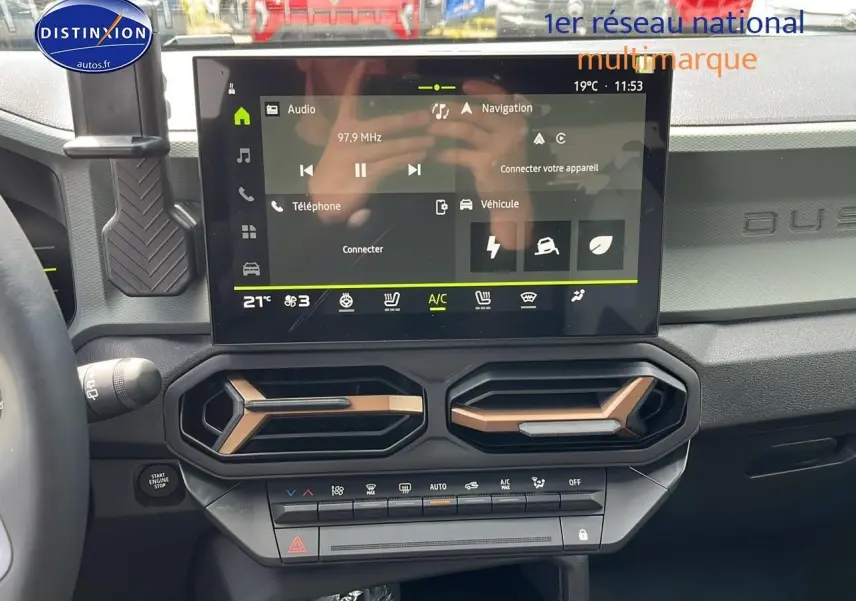 Vue intérieure du tableau de bord du Dacia Duster 2025 avec écran tactile et aérateurs hexagonaux noirs et bronze.