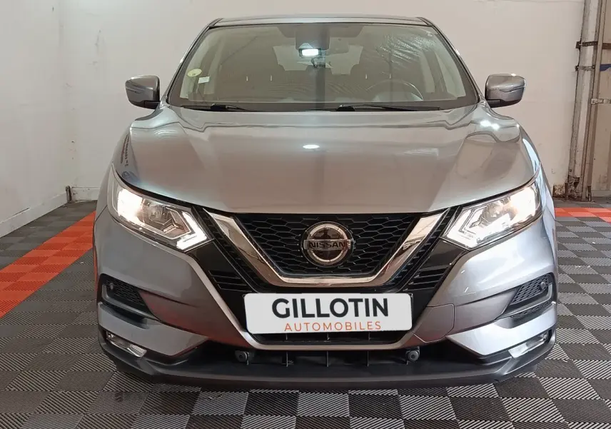 Vue frontale d'un Nissan Qashqai gris clair 2019 avec phares allumés et calandre chromée visible en intérieur.