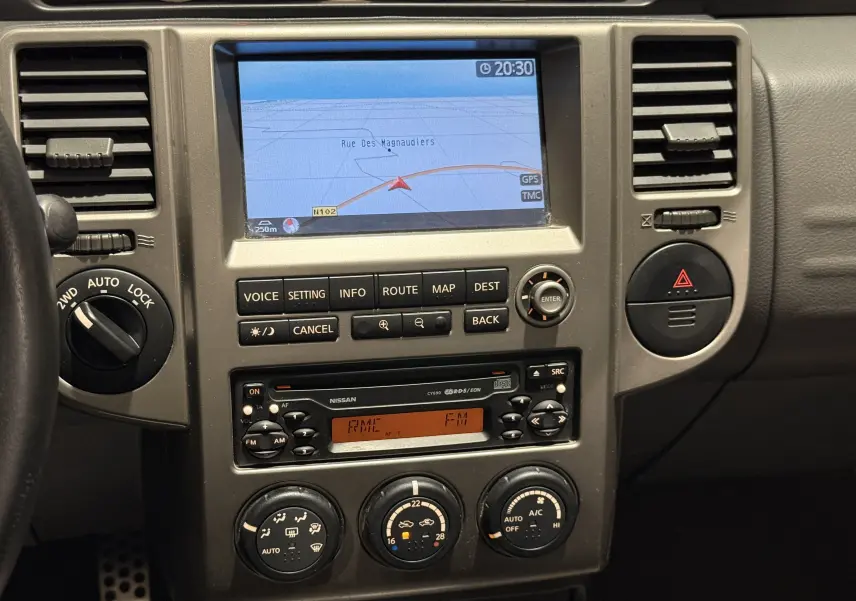 Vue rapprochée du tableau de bord du Nissan X-TRAIL Columbia gris 2006, avec écran GPS et commandes manuelles.
