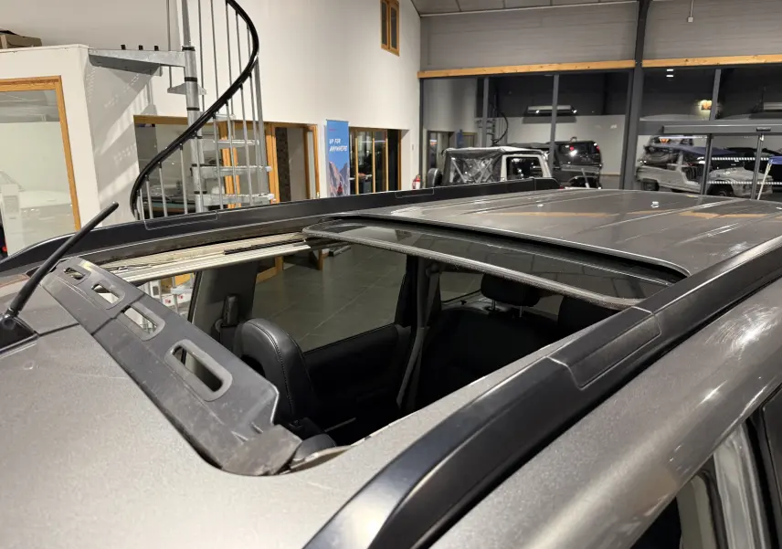 Toit ouvrant ouvert vu en plongée sur un Nissan X-TRAIL Columbia gris 2006 dans un showroom.