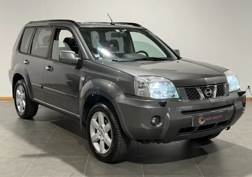 Nissan X-Trail Columbia gris vu en 3/4 avant droit, phares allumés et jantes alliage distinctives visibles.