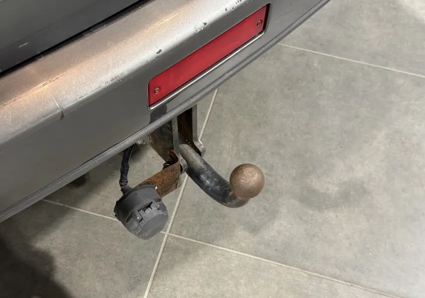 Gros plan sur l'attelage rouillé sous le pare-chocs arrière gris du Nissan X-Trail Columbia 2006.