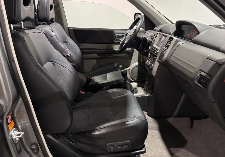 Vue intérieure côté conducteur du Nissan X-TRAIL Columbia 2006, sièges cuir noirs et tableau de bord gris.