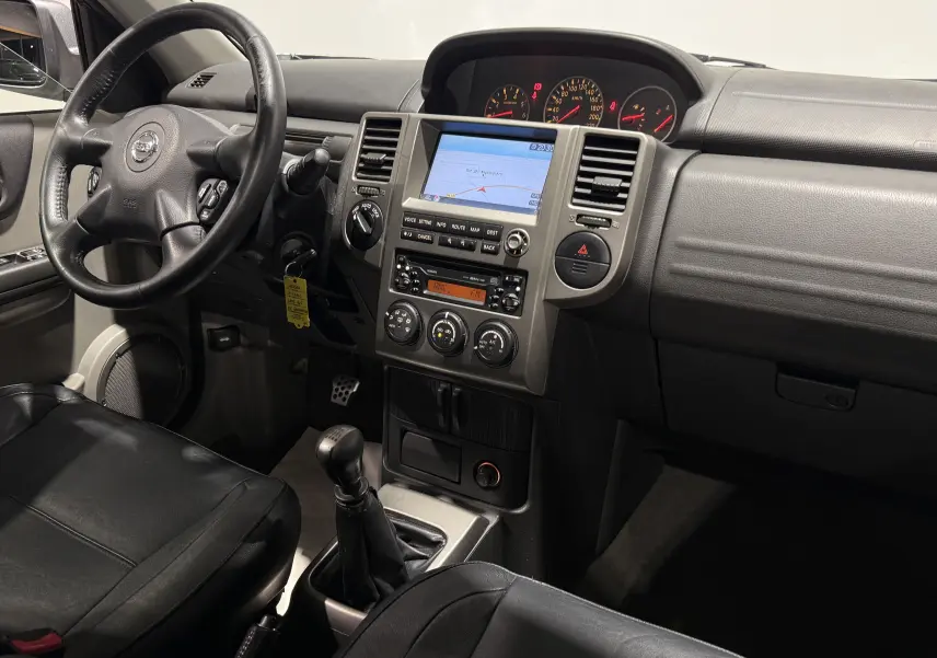 Vue intérieure côté conducteur du Nissan X-TRAIL Columbia 2006, montrant le tableau de bord noir avec écran GPS et boîte manuelle.