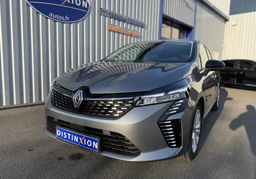 Renault Clio V gris schiste métal vue 3/4 avant droit, avec calandre noire et feux LED distinctifs allumés.