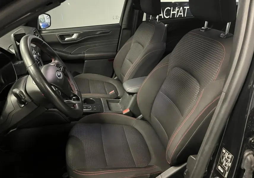 Intérieur avant du Ford Kuga noir 2022, sièges sport tissu noir avec surpiqûres rouges et volant ST-Line à méplat.