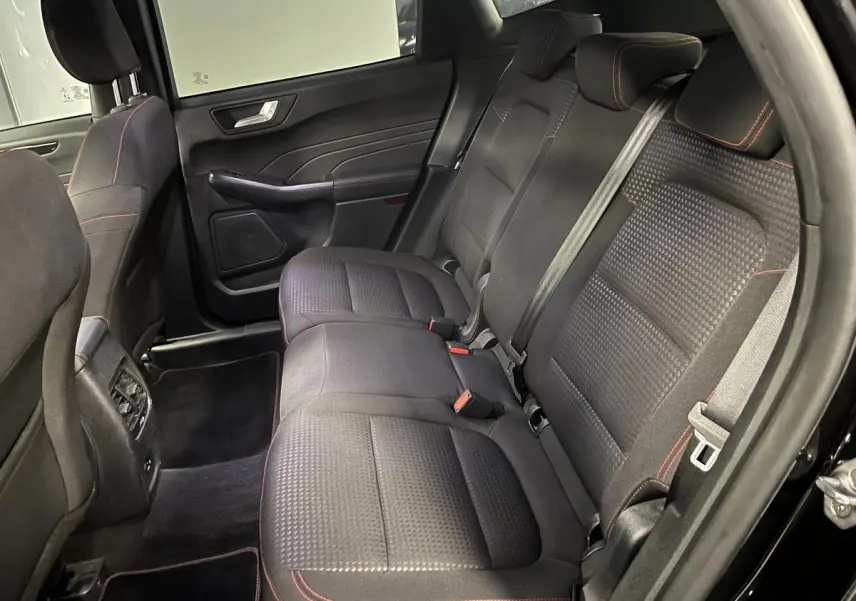 Vue intérieure arrière côté droit du Ford Kuga noir 2022, sièges tissu noir avec surpiqûres rouges et ceintures de sécurité visibles.