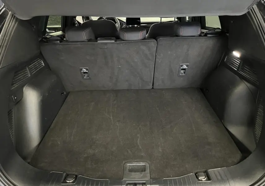Coffre noir spacieux du Ford Kuga 2022 avec banquette arrière rabattue et éclairage intérieur allumé.