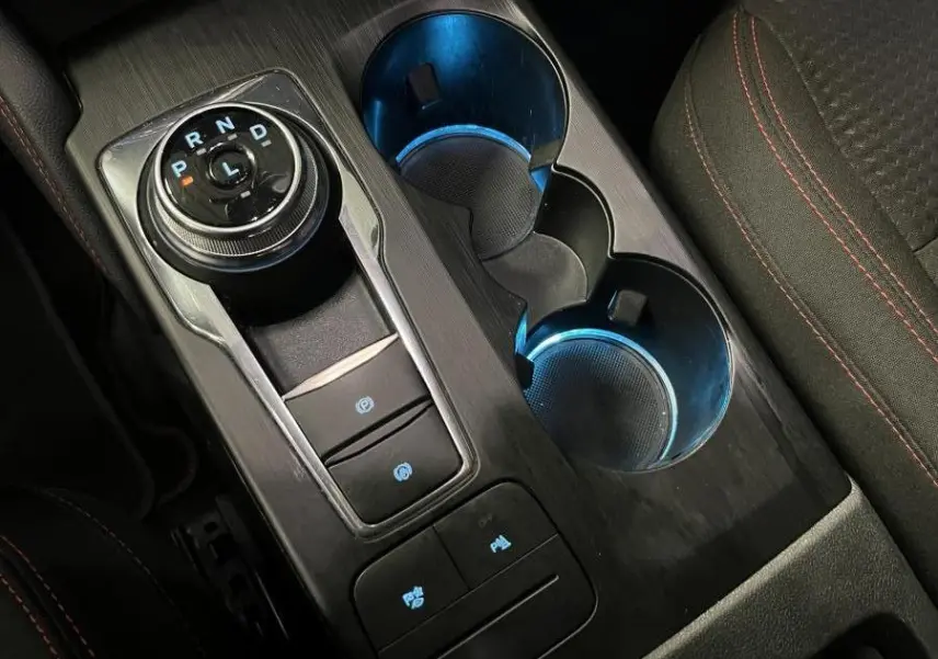 Vue rapprochée de la console centrale noire du Ford Kuga 2022 avec sélecteur rotatif et éclairage bleu des porte-gobelets.