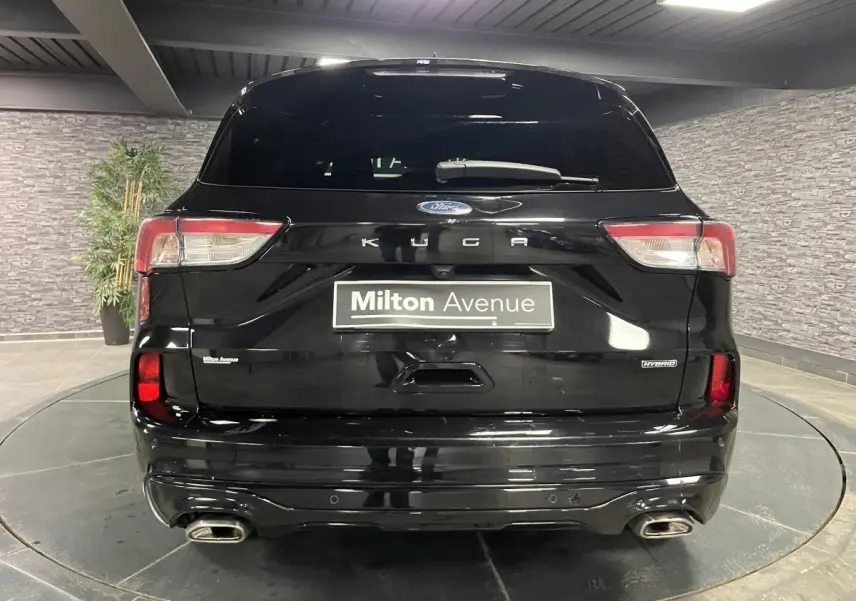 Vue arrière d'un Ford Kuga noir avec double sortie d'échappement et badges Hybrid et Kuga visibles.