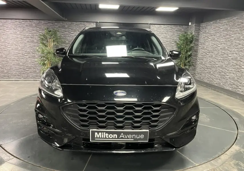 Vue frontale d'un Ford Kuga noir 2022 avec calandre hexagonale et badge Ford visible en intérieur showroom.