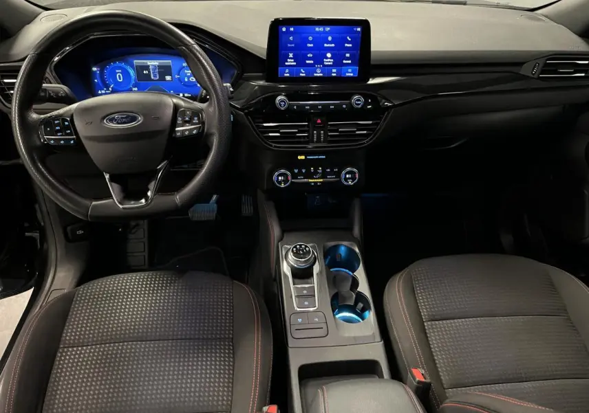 Vue intérieure avant du Ford Kuga noir 2022, tableau de bord numérique et console centrale avec sélecteur rotatif.