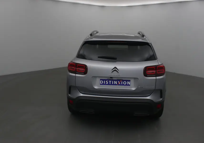 Vue arrière d'un Citroën C5 Aircross gris Artense avec feux arrière rouges et toit équipé de barres de toit.