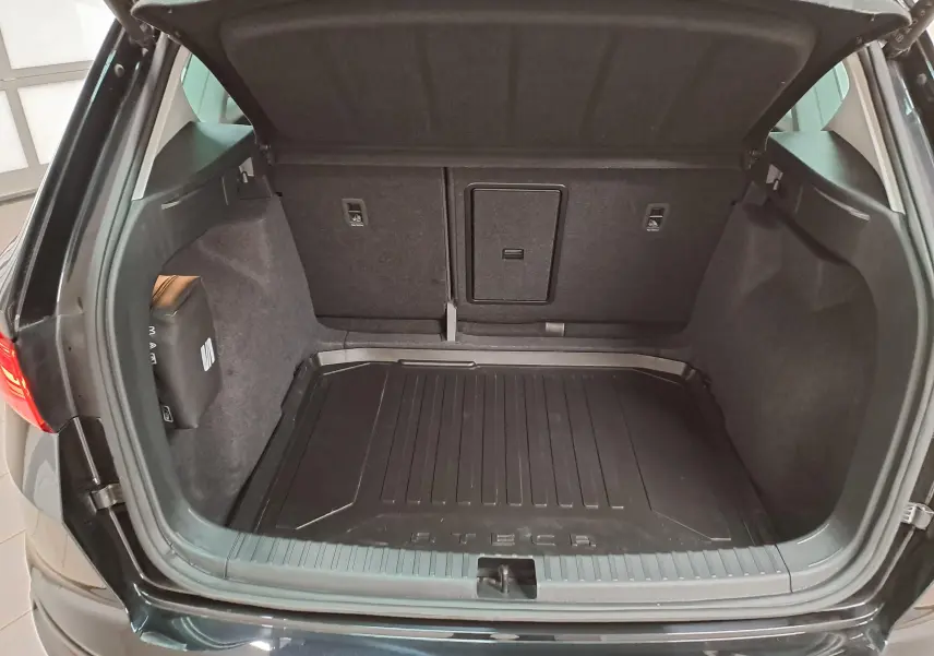 Coffre ouvert vu de l'arrière d'un SEAT Ateca Noir Minuit 2023, avec tapis de coffre et sellerie sombre visible.