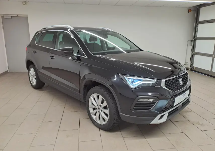 Vue 3/4 avant droite d'un SEAT Ateca 2023 noir minuit avec phares allumés dans un garage intérieur.