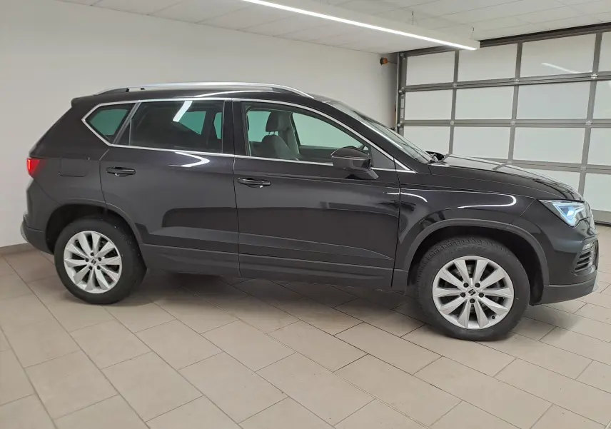Vue de profil côté gauche d’un SEAT Ateca 2023 noir minuit avec jantes alliage et vitres teintées dans un garage.