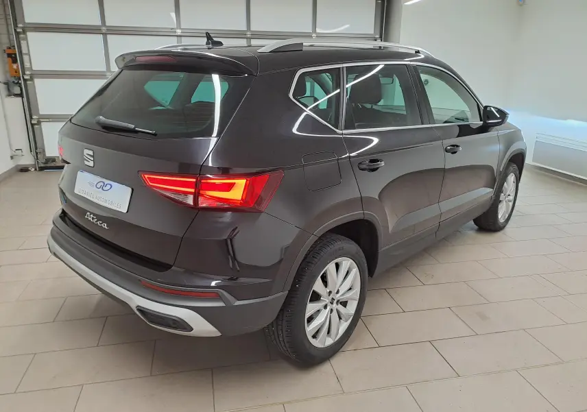 Vue 3/4 arrière droite d'un SEAT Ateca 2023 noir minuit avec feux arrière allumés dans un garage lumineux.