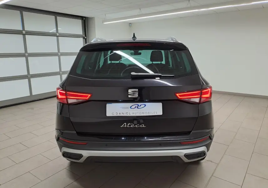 Vue arrière d'un SEAT Ateca noir minuit 2023 avec feux allumés dans un garage intérieur lumineux.