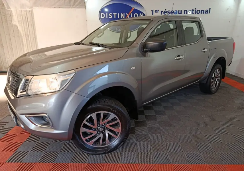 Nissan Navara Double-Cab gris clair vu en 3/4 avant droit, avec jantes alliage et benne pick-up visible.