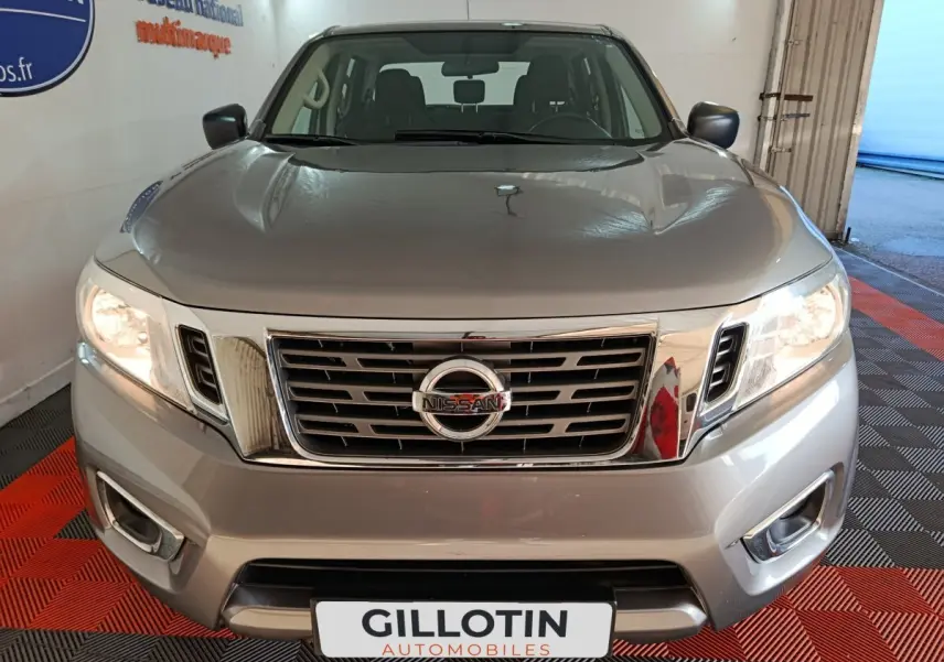 Vue avant d'un Nissan Navara Double-Cab gris clair, mettant en valeur sa calandre chromée et ses phares allumés.