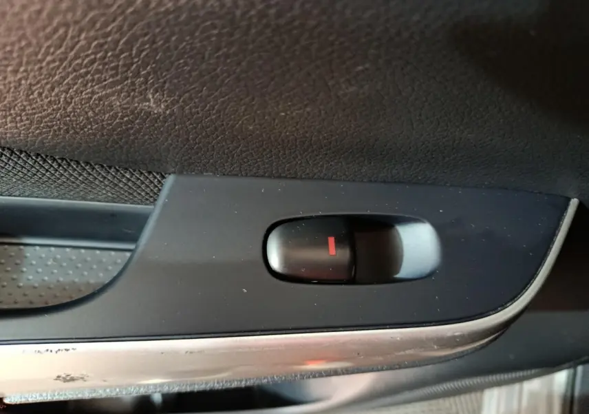 Gros plan sur le bouton de verrouillage central noir avec indicateur rouge, sur la porte intérieure d'un Nissan Navara gris clair.