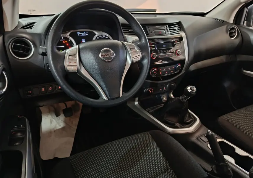 Vue intérieure centrée sur le volant multifonctions et la console centrale d’un Nissan Navara 2018, sièges noirs.