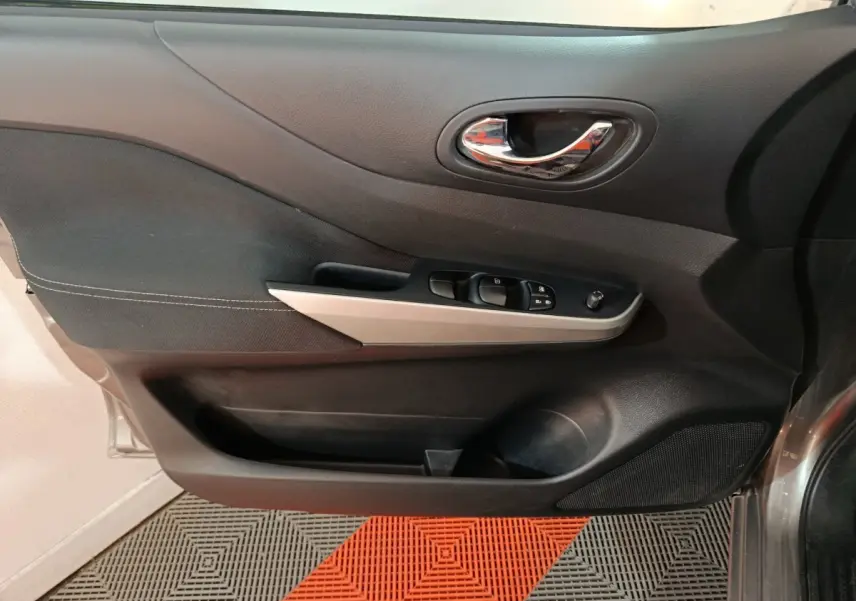 Vue intérieure côté gauche de la porte avant d'un Nissan Navara gris clair avec commandes de vitres et poignée chromée.