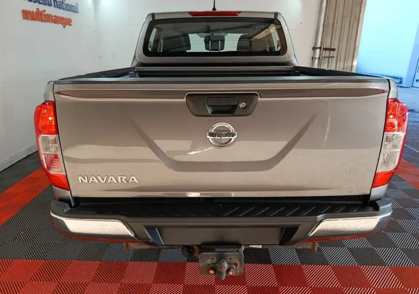 Vue arrière d’un Nissan Navara gris clair avec benne pick-up et attelage visible dans un garage.