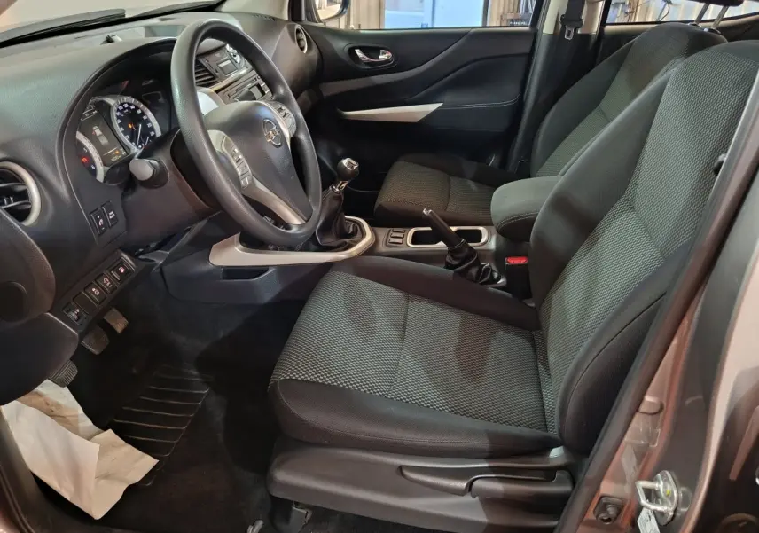 Vue intérieure côté conducteur du Nissan Navara gris clair 2018, montrant le volant multifonctions et la boîte manuelle.