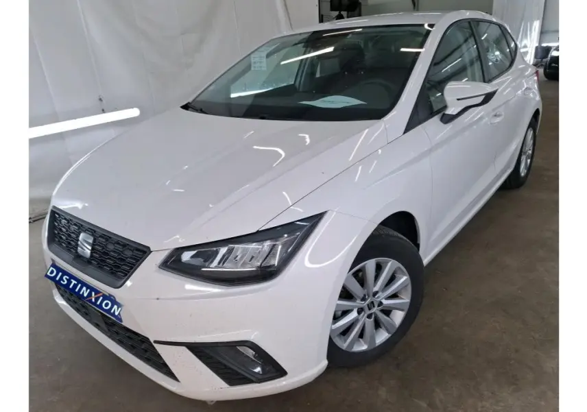 Vue 3/4 avant droite d'une SEAT Ibiza blanche 5 portes exposée en showroom avec jantes alliage et calandre noire.