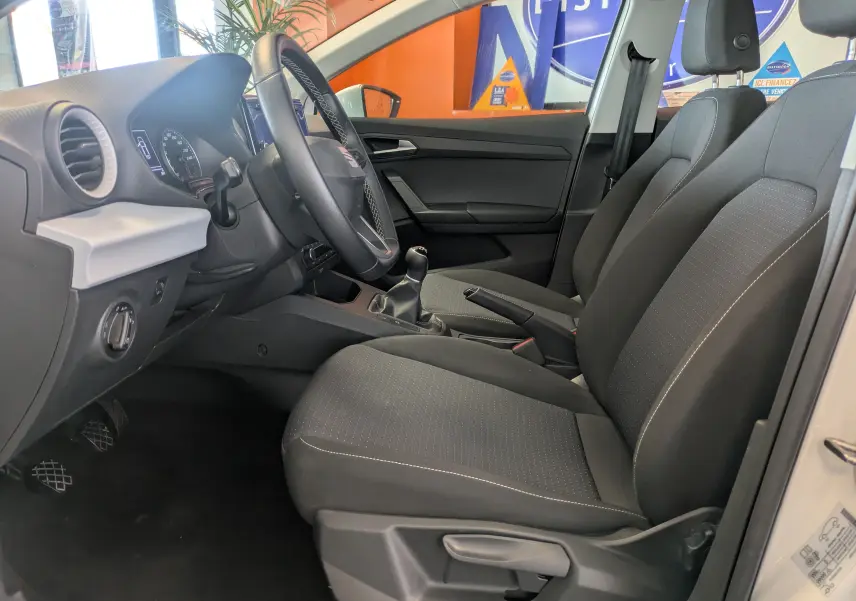 Vue intérieure côté conducteur de la SEAT Ibiza blanche 5 portes, montrant les sièges noirs et la boîte manuelle.
