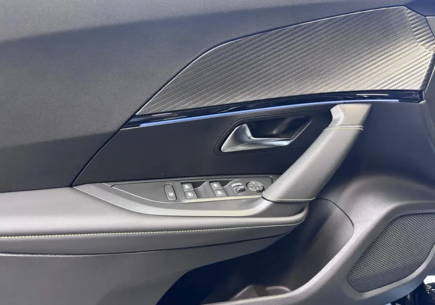 Détail de la porte avant gauche noire du Peugeot 2008 1.2i Hybrid 2026 avec surpiqûres vertes et insert carbone.
