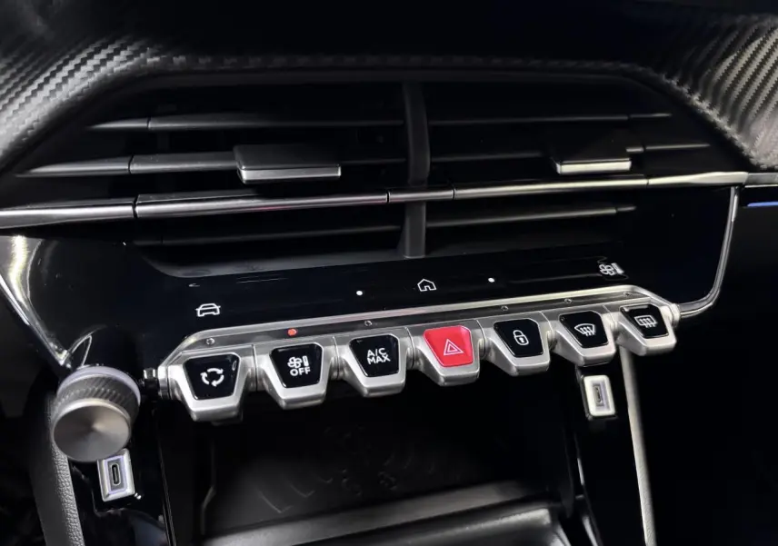 Gros plan sur la console centrale du Peugeot 2008 1.2i Hybrid GT 2026, avec commandes climatisation et finition carbone.
