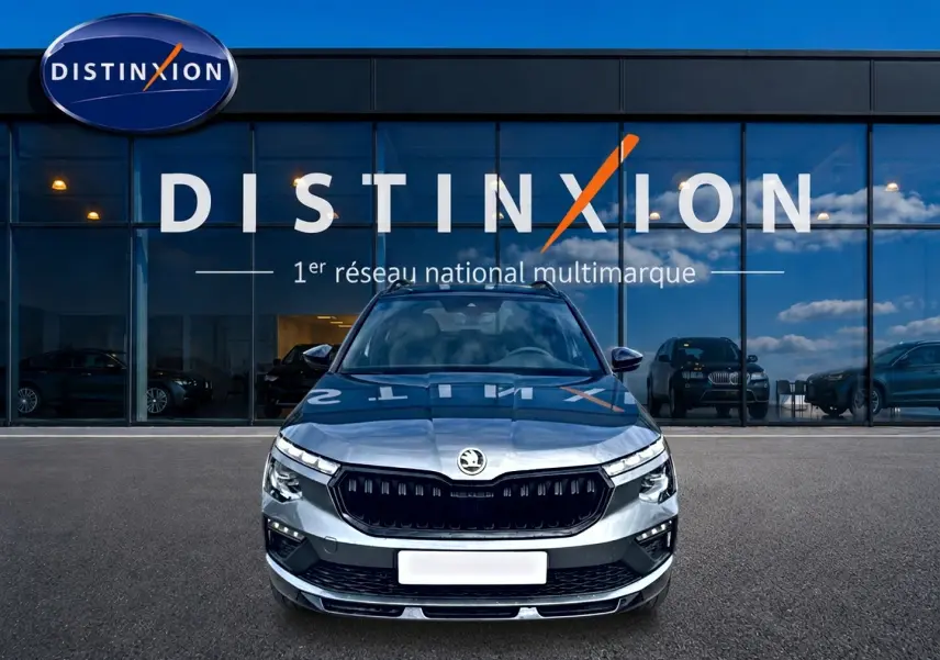 Vue frontale d'un Skoda Kamiq gris graphite garé devant une vitrine avec logo Distinxion en arrière-plan.