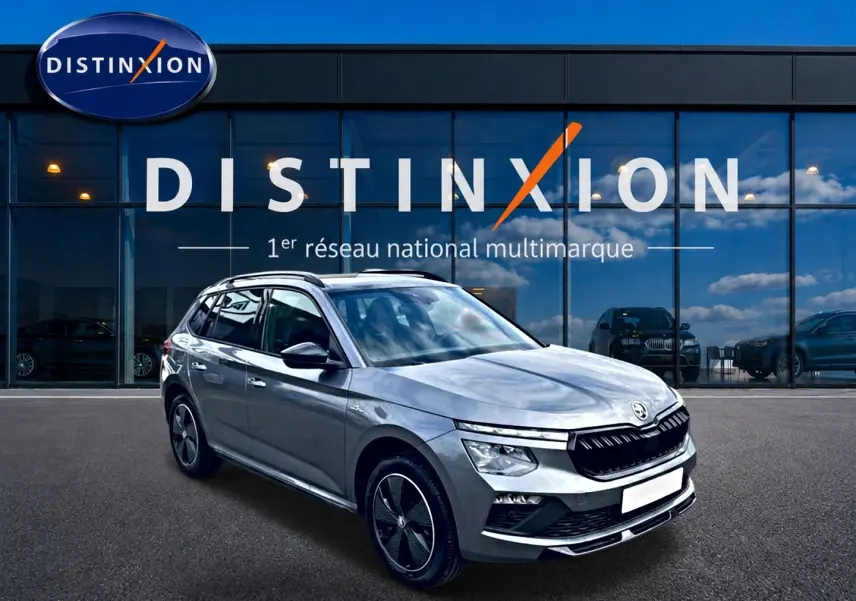 Skoda Kamiq gris graphite en 3/4 avant droit, avec jantes alu et toit panoramique visible, devant un showroom Distinxion.