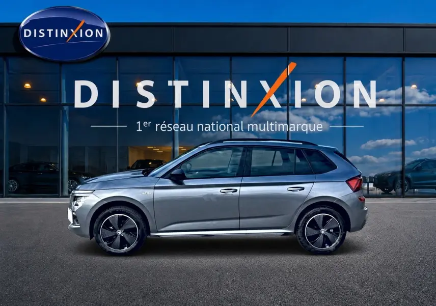 Vue latérale droite du Skoda Kamiq gris graphite avec jantes alu noires et toit panoramique en verre, devant une vitrine Distinxion.