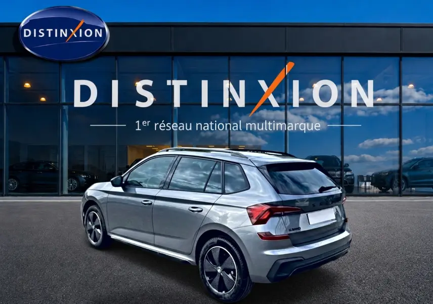 Vue 3/4 arrière droite d’un Skoda Kamiq gris graphite avec jantes alu noires devant une vitrine Distinxion.
