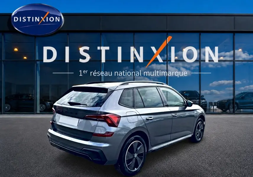 Vue 3/4 arrière droite d'un Skoda Kamiq gris graphite avec jantes alu et toit panoramique devant un showroom Distinxion.