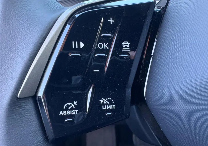 Gros plan sur les commandes noires du volant du Peugeot 5008 Hybrid 2025, avec boutons d'assistance et limitation de vitesse.